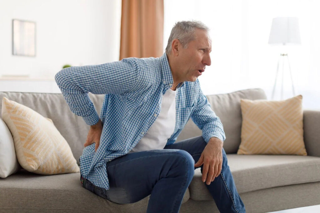 An elderly man struggling with back pain, highlighting the need for a massage for sciatica.