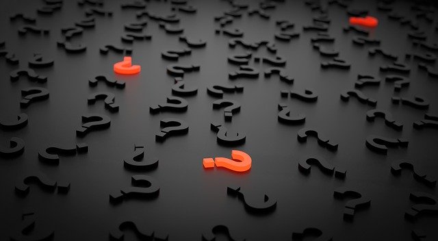 A dark surface scattered with numerous black question marks, with a few glowing red question marks standing out, symbolizing uncertainty and the search for answers.