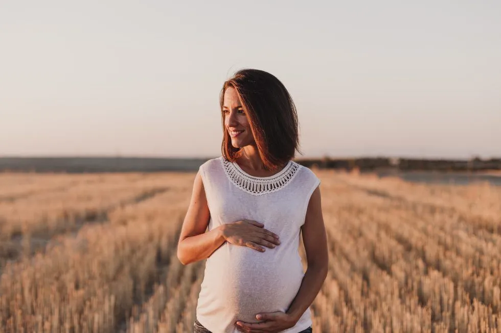 Happy pregnant woman outdoors, gently holding her belly, symbolizing wellness and pregnancy chiropractor care.