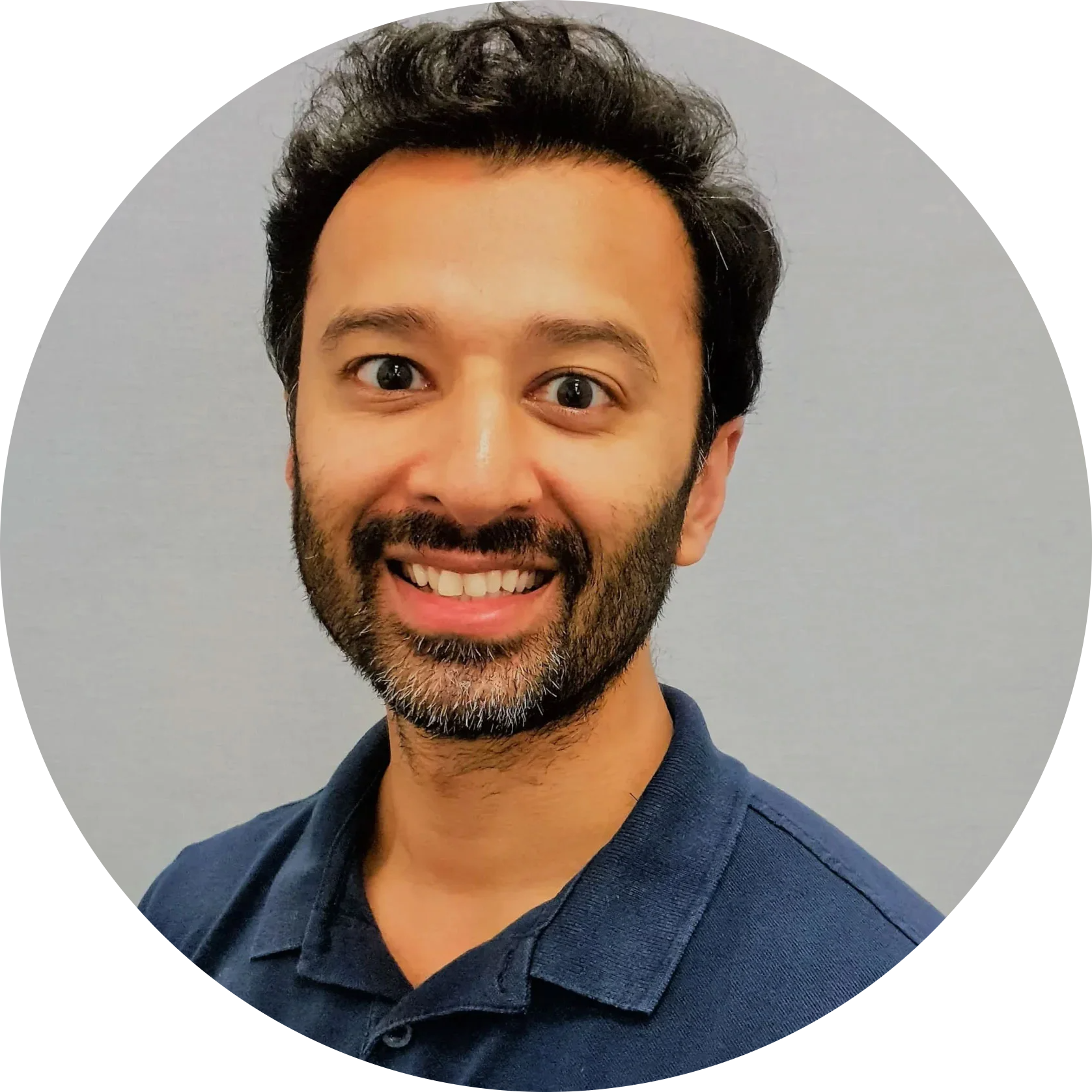 Portrait of a smiling man with dark hair and beard wearing a navy polo shirt, circular crop, light gray background.